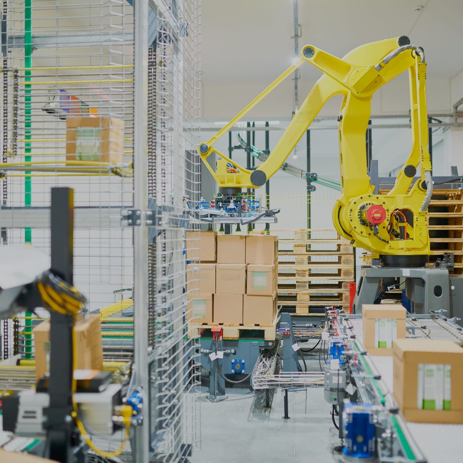 Gele palletiseerrobot boven een inpaklijn, met transportbanen, dozen op een pallet en een veiligheidshek eromheen.
